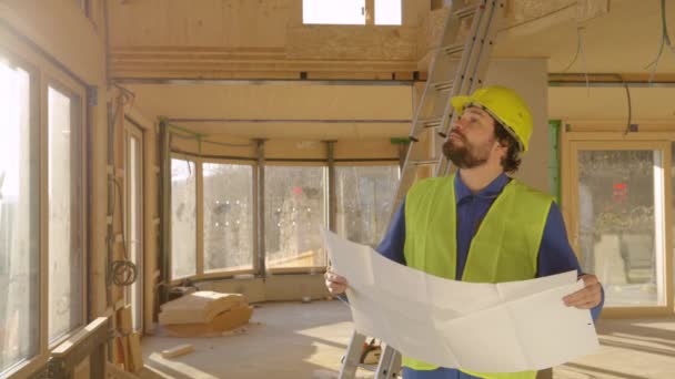 COPY SPACE: Male architect looks at his plans and observes an unfinished house. — Stock Video
