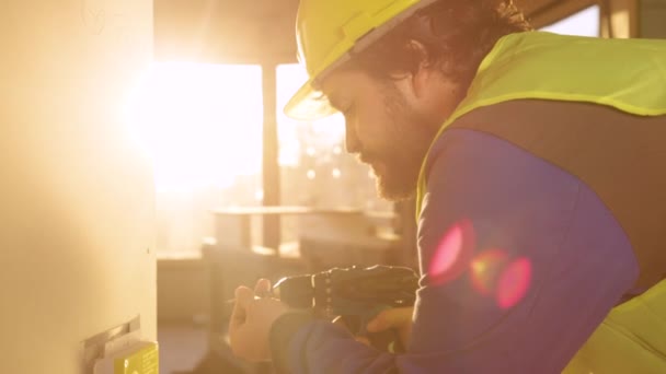 LENS FLARE: Reggeli napsugarak ragyog munkavállaló fúró csavarok egy fali panel — Stock videók