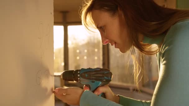 LENS FLARE: Woman is doing a man's job by unscrewing bolts out of a plaster wall — Stock Video