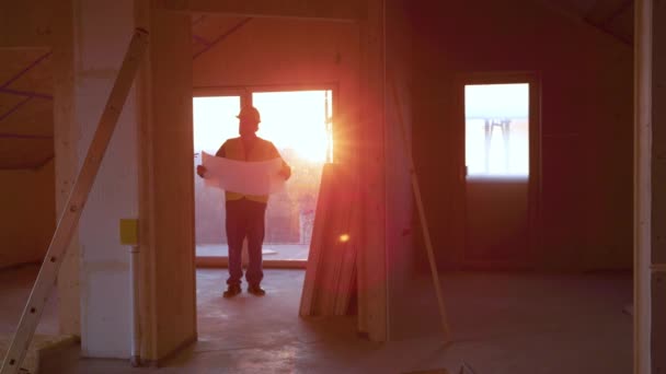 LENS FLARE: Αρχιτέκτονας περπατά γύρω από ένα σπίτι υπό κατασκευή στο χρυσό ηλιοβασίλεμα. — Αρχείο Βίντεο