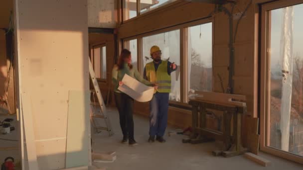 Arkitekt håller sina planer ger kvinnan en rundtur i hennes hus under uppbyggnad. — Stockvideo