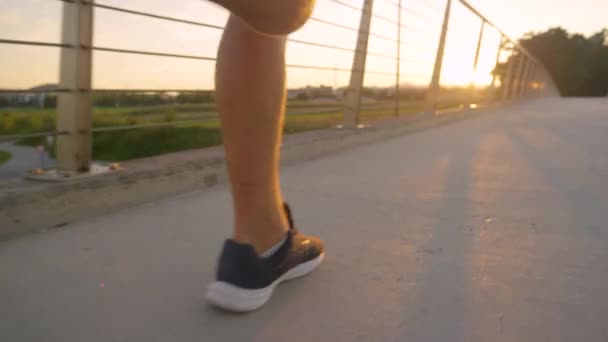 LOW ANGLE Young man jogs across a bridge and towards the beautiful golden sunset — Stock Video