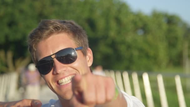 PORTRAIT: Usmívající se mladý student ukazuje na kameru v zábavný den v parku. — Stock video