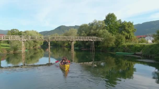 DRONE: Group of young tourists on canoeing trip paddle under a wooden bridge — Stock Video