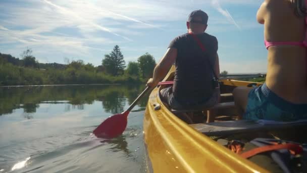 FECHAR-SE: Jovem e homem remam uma canoa ao longo de um rio tranquilo no dia ensolarado — Vídeo de Stock