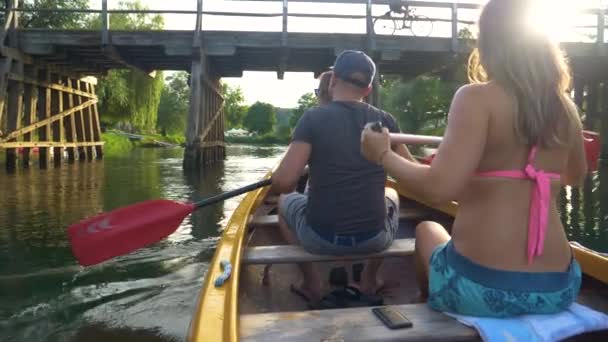 CERRAR: Hombre y mujer reman en una canoa a lo largo de un río tranquilo y bajo un puente — Vídeos de Stock