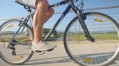 Kot şortlu tanınmayan bir adam köprüde bisiklet pedalları çeviriyor..