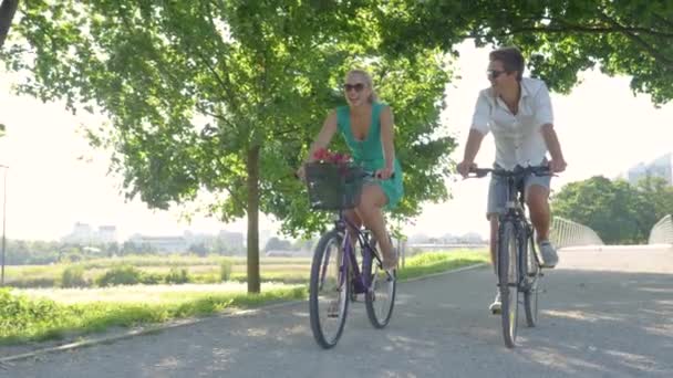 LENS FLARE: Fotografia cinematográfica de um casal andando de bicicleta ao longo de uma avenida iluminada pelo sol. — Vídeo de Stock