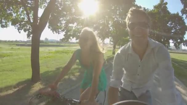 SELFIE: Los rayos del sol brillan en la pareja de turistas felices montando bicicletas alrededor de un parque — Vídeos de Stock