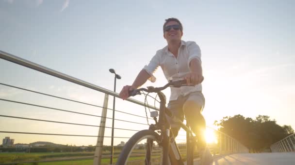 LENS FLARE: Homem despreocupado desfruta de uma noite ensolarada de verão, andando de bicicleta. — Vídeo de Stock