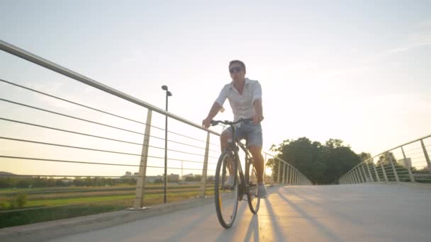 LOW ANGLE: Carefree guy whistles while riding a bike on a sunny summer morning. — Stock Video