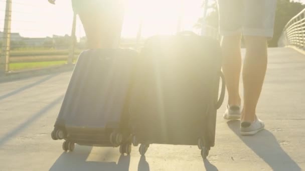 LENS FLARE: Toeristisch koppel trekt reistassen achter zich aan op weg naar het vliegveld — Stockvideo