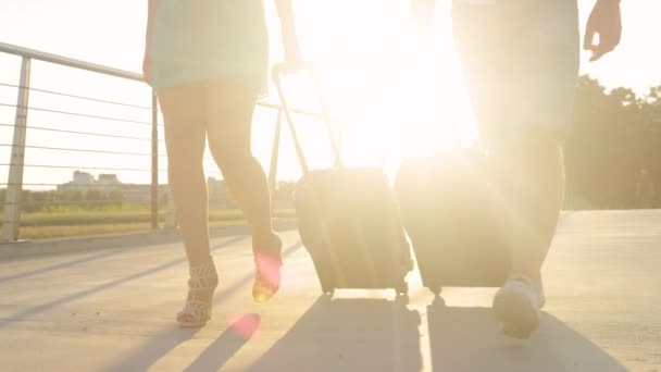 LOW ANGLE: Summer sunrise shines on a tourist couple walking with their luggage. — Stock Video