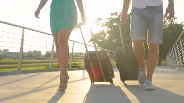 LENS FLARE: Golden light shines on tourist couple pulling suitcases behind them. — Stock Video