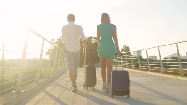 LENS FLARE: Jonge toeristen op weg naar de luchthaven lopen over een viaduct. — Stockvideo