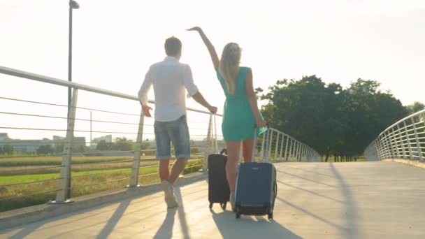 LENS FLARE: Happy woman walking to airport with boyfriend outstretches her arm. — Stock Video