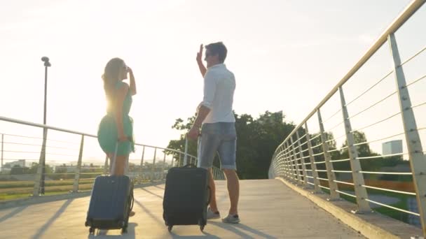 FLARE DE LA LENTE: Mujer y novio colocan cinco mientras caminan al aeropuerto con el equipaje. — Vídeos de Stock