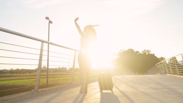 LENS FLARE: Menina feliz gira em torno de sua mala enquanto caminha para o aeroporto — Vídeo de Stock