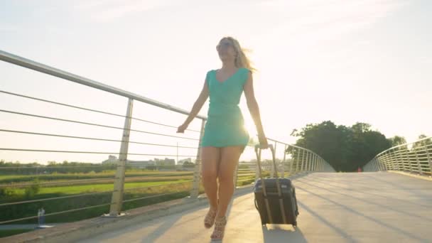 LENS FLARE: Gorgeous woman in heels walks across an overpass with a suitcase. — Stock Video