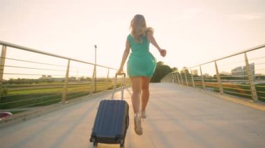 Topuklu ayakkabılı turist kız uçağına yetişmek için valiziyle koşar..
