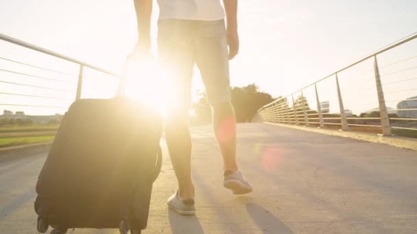 ÁNGULO BAJO Hombre irreconocible en pantalones cortos camina a través de un paso elevado con su equipaje — Vídeos de Stock