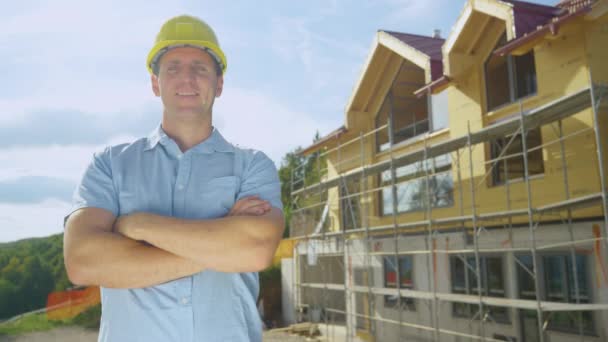 PORTRAIT: Ο ανάδοχος χαμογελά μπροστά σε ένα σύγχρονο υπό κατασκευή σπίτι. — Αρχείο Βίντεο