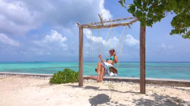 CERRAR: Chica viajera disfrutando de un día soleado balanceándose en una playa de arena. — Vídeo de stock