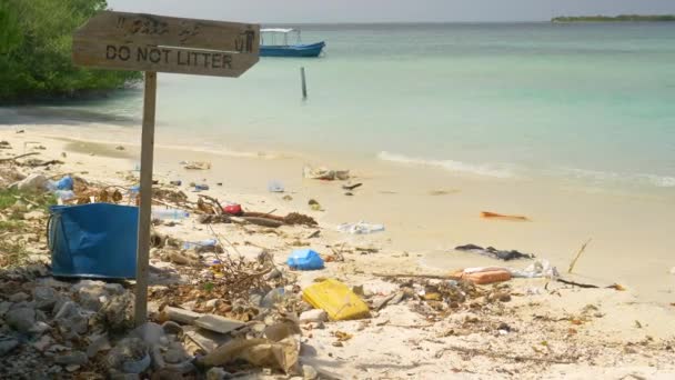 CERRAR: letrero de madera prohíbe tirar basura en una playa de arena blanca llena de basura — Vídeo de stock