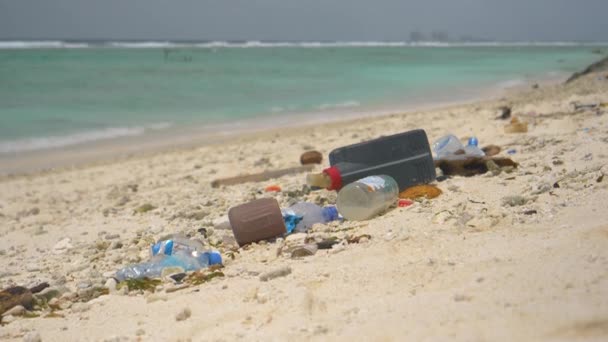 CLOSE UP: Plastic bussen en flessen zijn verspreid over de tropische kust. — Stockvideo