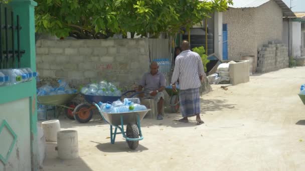 ZAMKNIJ: Dwóch miejscowych mężczyzn czeka na dostawę wody słodkiej z pustymi butelkami wody. — Wideo stockowe