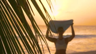 Mutlu bir kadın kumsaldan kafasında sörf tahtasıyla gelir..