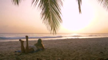 Tanınmayan turist kız plajda dinleniyor ve gün batımını izliyor.