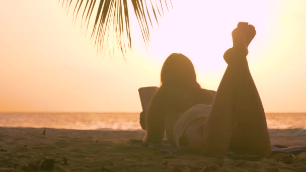 LENS FLARE: Chica turística disfruta de una noche soleada en la playa leyendo un libro . — Vídeo de stock