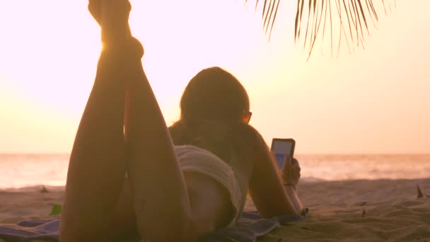 LOSE UP: Turisttjejen njuter av sommarkväll på stranden genom att mixtra med sin telefon — Stockvideo