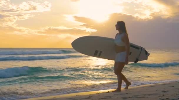 COPY SPACE: чудова туристична дівчина прогулюється піщаним пляжем з дошкою для серфінгу — стокове відео