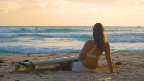 CHIUDI: Turista femminile si siede sulla spiaggia di sabbia e guarda i surfisti al tramonto — Video Stock