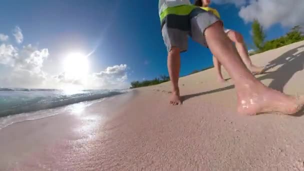 LOW ANGLE: Oigenkännlig turist par promenader barfota längs tropiska stranden. — Stockvideo