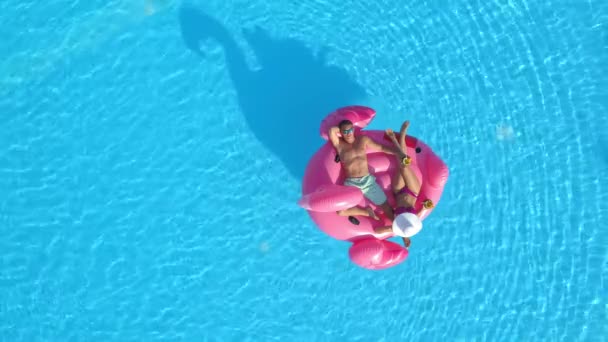 TOP DOWN: Man en vriendin op zomervakantie chill op een roze flamingo floatie — Stockvideo