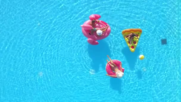 AERIAL: Flying above a group of friends relaxing on floaties during a pool party — Stock Video