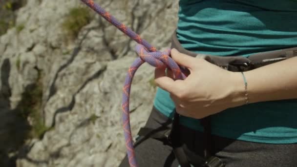 CLOSE UP: Kvinna fäster ett rep på selen innan du klättrar upp för en klippa. — Stockvideo