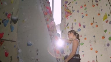 Genç beyaz kadın kurşunu renkli bir yapay duvara tırmanıyor..