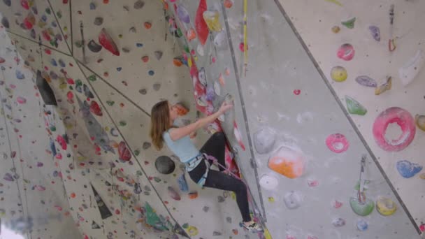 CLOSE UP: Girl grips on to a pinch hold while she loops her rope into carabiner. — Stock Video