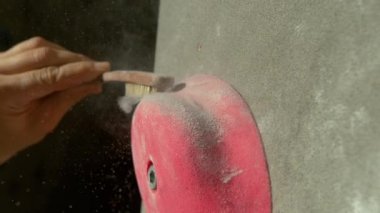 Tanınmayan kaya tırmanışçısı sıkı bir fırçayla pembe bir tutuşu temizliyor.