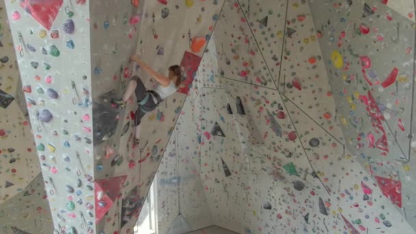 AERIAL: Vliegen in de buurt van een atletische vrouw indoor lood klimmen op een moeilijke route. — Stockvideo