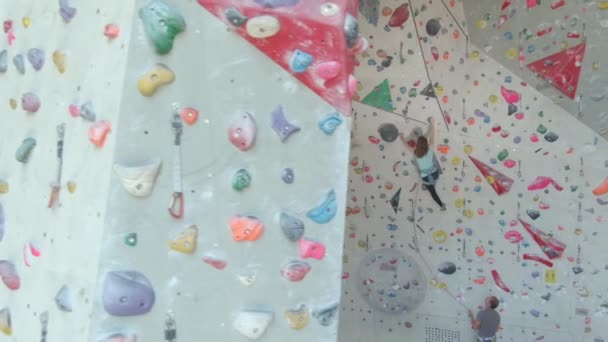 AERIAL: Unrecognizable man belays a young teenager climbing up an indoor wall. — Stock Video