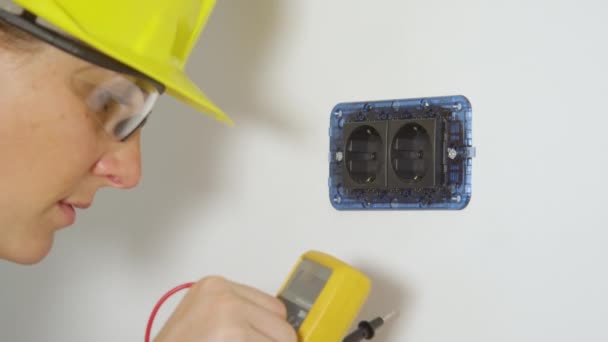 CHIUSURA: Una giovane elettricista donna controlla una presa con un nuovo multimetro. — Video Stock