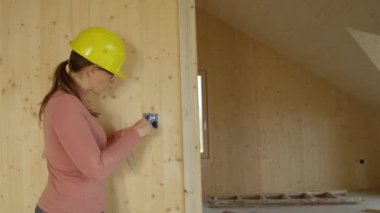 Genç bayan elektrikçi, ahşap bir duvara prizden bir çerçeve takıyor.