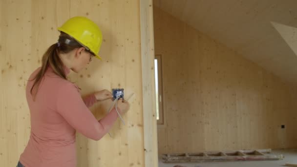 ΚΛΕΙΣΙΜΟ: Νεαρή γυναίκα ηλεκτρολόγος βιδώνει ένα πλαίσιο εξόδου σε έναν ξύλινο τοίχο — Αρχείο Βίντεο