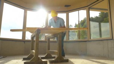 Marangoz bir kalas ölçer ve onun planları ile karşılaştırır.