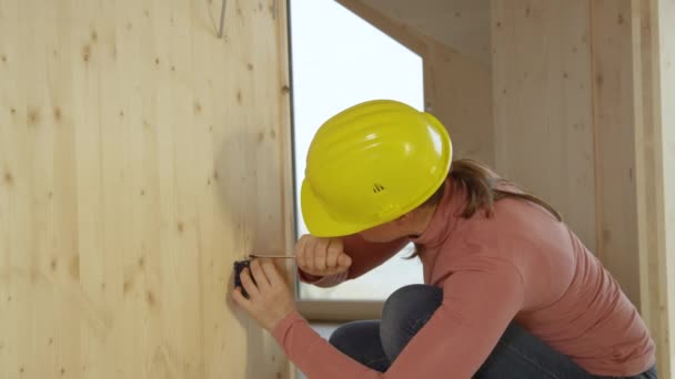 CLOSE UP: Ung kaukasisk kvinna hukar sig ner för att installera ett eluttag. — Stockvideo